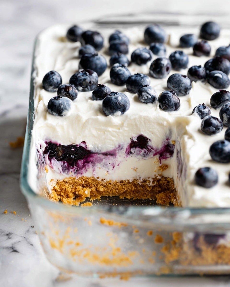 A square glass dish holds a three-layer dessert placed on a white marbled texture. The bottom layer is a crumbly, golden brown crust, rough in texture and slightly loose around the edges. The middle layer is a smooth, white cream mixed with dark purple blueberry swirls showing through slightly. The top layer is a thick, even spread of white cream, decorated with whole plump blueberries scattered across the surface. A large piece has been cut out from one corner, revealing the clear separation of each layer. Photo taken with an iphone --ar 4:5 --v 7