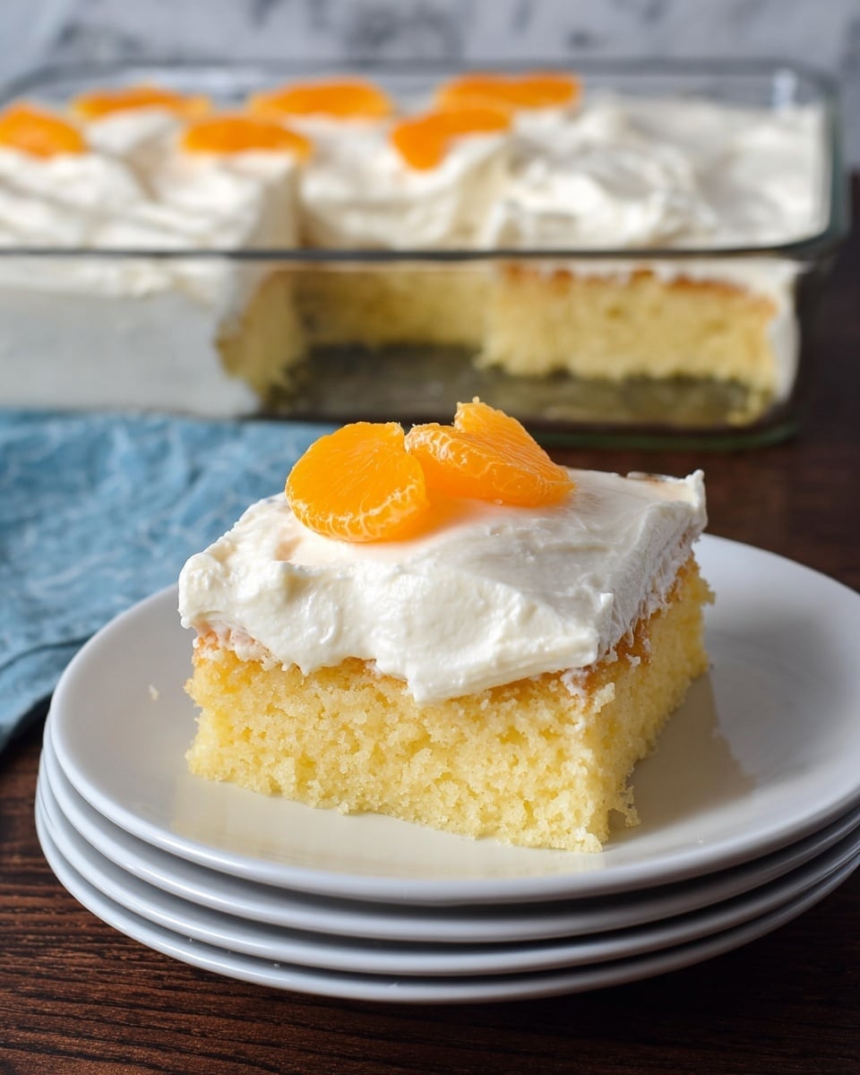 The image shows a square slice of yellow cake with a soft, moist texture as the bottom layer. On top, there is a thick, creamy white frosting spread evenly with some light, fluffy texture. Two bright orange mandarin segments sit on the center of the frosting, adding a pop of color. The slice is placed on a stack of three white plates, set on a dark wooden table with a white marbled texture background. In the back, part of a glass baking dish with the remaining frosted cake is visible. photo taken with an iphone --ar 4:5 --v 7