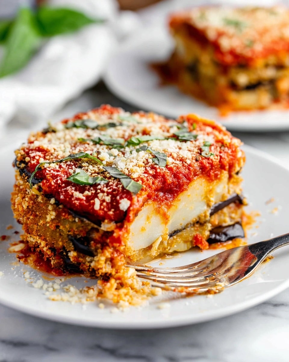 A close-up of a round slice of eggplant parmesan on a white plate placed on a white marbled surface. The dish has three visible layers: the bottom layer consists of thick white eggplant slices with dark purple skin, the middle layer shows melted creamy cheese mixed with bits of eggplant and sauce, and the top layer is covered with bright red tomato sauce, sprinkled with grated white cheese and green basil pieces. The edges of the slice are golden and slightly crispy. In the foreground, a fork is resting on the plate near the slice, and the background shows a blurred second plate with a similar slice. photo taken with an iphone --ar 4:5 --v 7