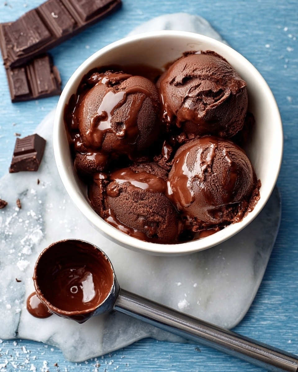 A round white bowl filled with four scoops of rich, dark chocolate ice cream, each scoop smooth with glossy melted chocolate drizzled on top, creating a shiny texture. Next to the bowl lies a metal ice cream scoop with some melted chocolate inside, resting on a white marbled surface. In the background, pieces of dark chocolate are placed casually on the surface, adding depth and context to the scene. photo taken with an iphone --ar 4:5 --v 7