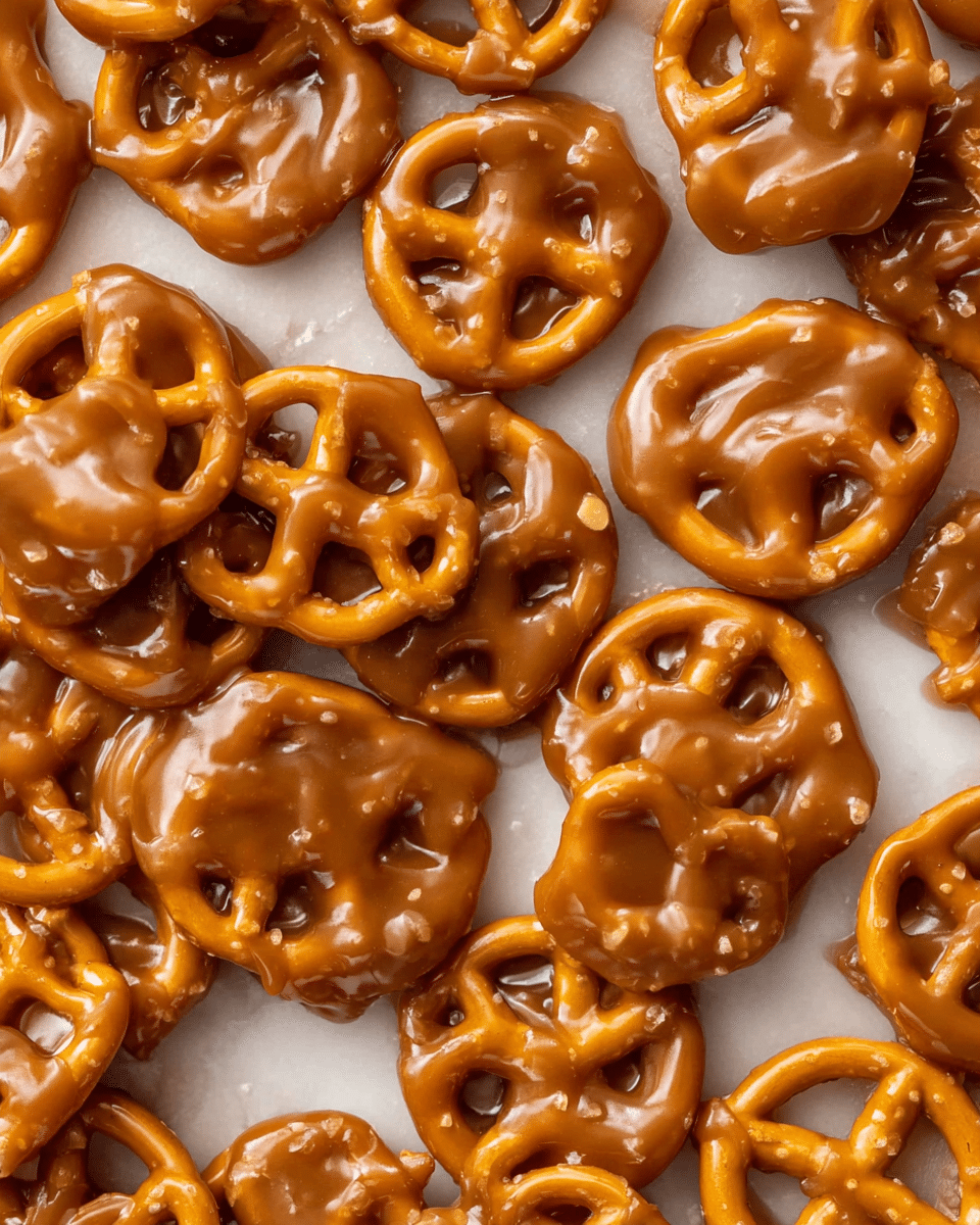A close-up image shows small pretzels coated in a thick, glossy caramel sauce. The caramel is shiny and covers each pretzel evenly, with some areas pooling slightly between pretzels, giving a sticky and rich texture. The pretzels are golden brown underneath the caramel, visible through the translucent coating. They are scattered loosely on a white marbled surface, filling the frame without any empty space. photo taken with an iphone --ar 4:5 --v 7