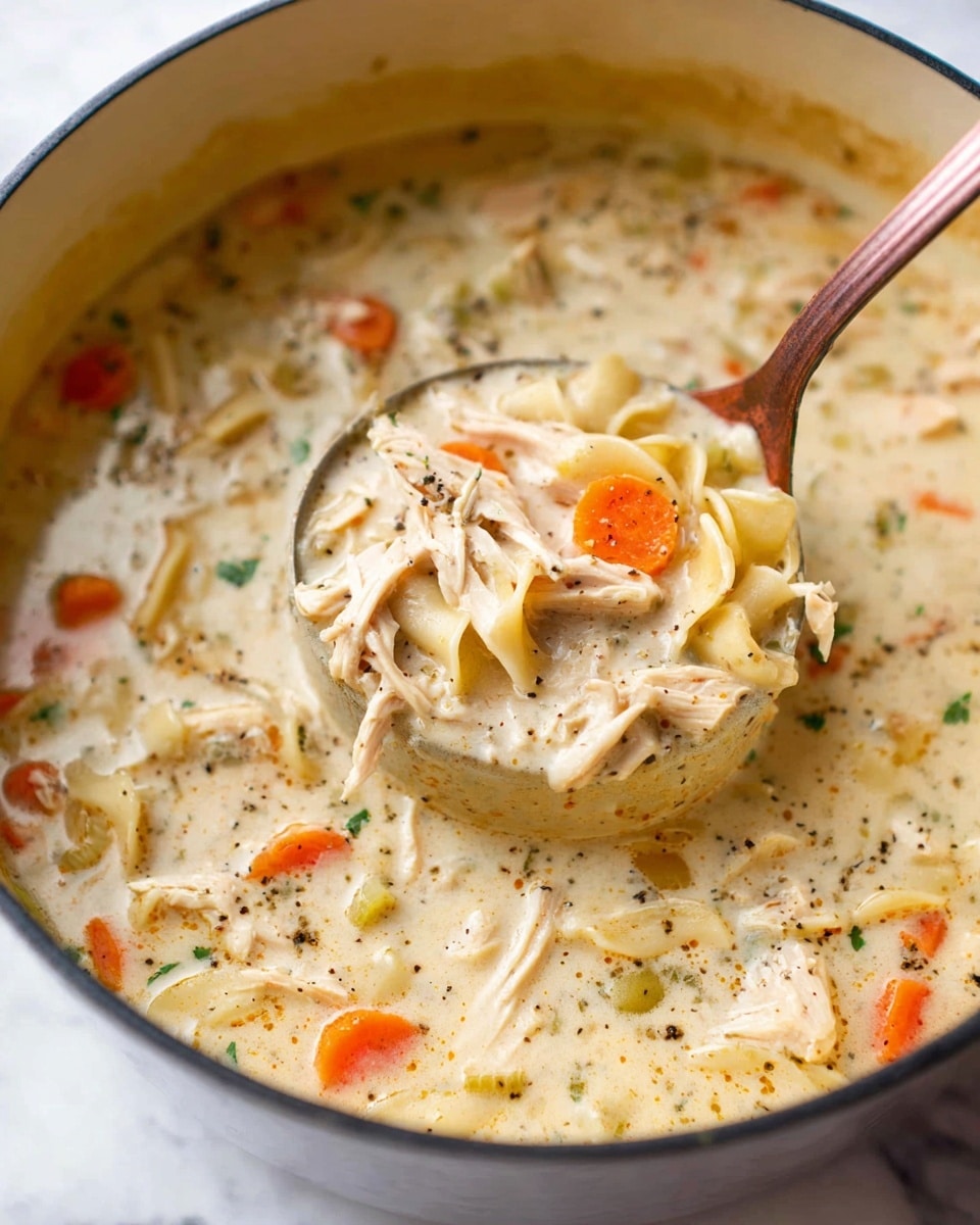 A close-up image of a pot filled with thick creamy chicken noodle soup showing a ladle lifting a portion. The soup has a creamy off-white base with visible pieces of shredded chicken in light brown, sliced carrots in bright orange, and small pieces of noodles in pale yellow. There are also specks of black pepper and herbs spread throughout the soup. The pot is round and white, contrasting with the soup’s colors. The background is a white marbled texture, giving a clean and bright look. photo taken with an iphone --ar 4:5 --v 7