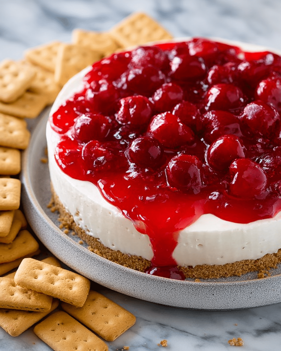 A deep round dish holds a two-layer dessert; the bottom layer is creamy white with a smooth, soft texture, and the top layer is bright red, glossy cherry topping with whole cherries visible, thickly covering the cream. The dish is white with a subtle grey rim, resting on a white marbled surface. Surrounding the dish are light golden vanilla wafer cookies stacked and scattered, along with rectangular brown graham crackers placed leaning against the dish on one side. Photo taken with an iphone --ar 4:5 --v 7