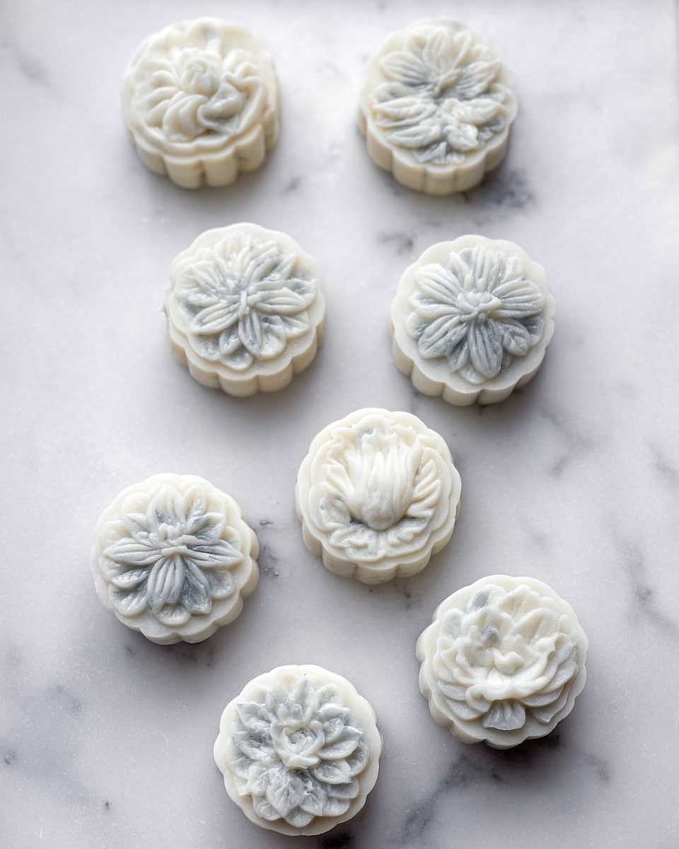 Several mooncakes are placed on a white marbled textured surface, each showing detailed floral and geometric patterns on top. The mooncakes have a frosty, soft texture with light gray and white colors mixed throughout, giving a slightly translucent, icy look. Small black sesame seeds are scattered around them on crinkled white paper that covers the surface. The shapes of the mooncakes include round and hexagonal, all with raised edges and intricate designs, looking delicate and cool. photo taken with an iphone --ar 4:5 --v 7