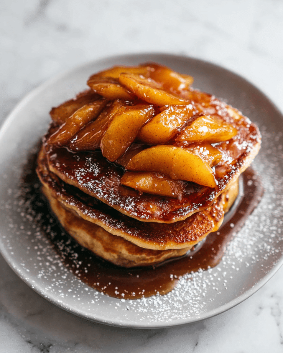 A stack of three thick, golden-brown pancakes sits on a white plate. On top of the stack, there is a layer of soft, warm apple slices cooked in syrup, shiny with a dark caramel glaze that lightly drips over the edges. The pancakes have a slightly crispy edge with a soft texture inside. Around the plate, a few sprinkles of powdered sugar add a delicate touch. The plate is placed on a white marbled textured surface. photo taken with an iphone --ar 4:5 --v 7