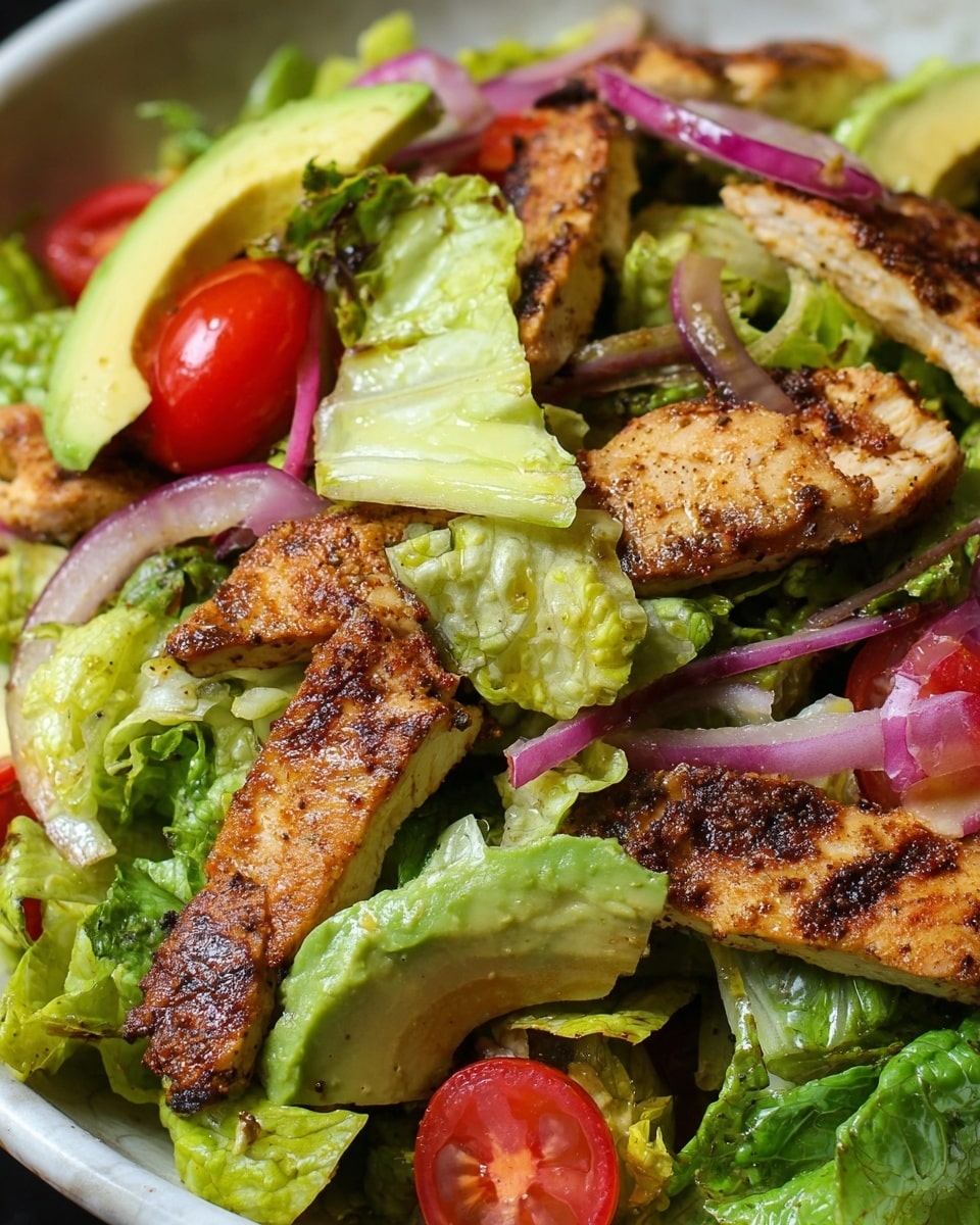 A close-up view of a salad shows three main layers: bright green romaine lettuce with a light, crunchy texture, juicy red cherry tomato halves scattered throughout, and grilled chicken strips with a browned, slightly charred surface positioned on top. There are also slices of pale yellow avocado and thin rings of purple-red onion adding a fresh and colorful touch, all mixed and lightly coated with a glossy dressing. The background is a white marbled texture. photo taken with an iphone --ar 4:5 --v 7