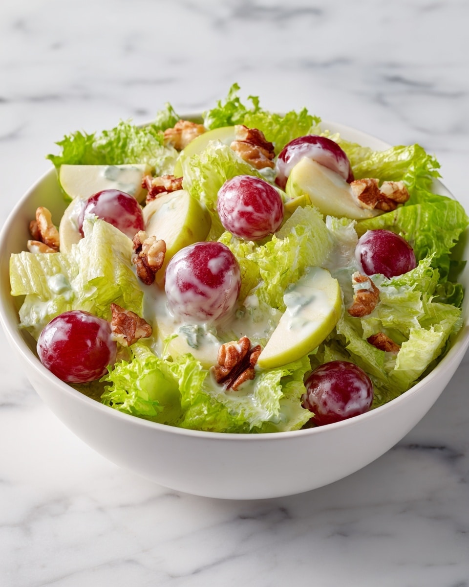 A white bowl holds a fresh-looking salad with several layers. The base layer is bright green leafy lettuce with ruffled edges, surrounding the other ingredients. On top, there are chunks of pale yellow apple pieces mixed with light green celery slices, round halves of red grapes, and light brown walnut pieces, all coated in a creamy white dressing, giving the salad a glossy look. The bowl sits on a white marbled surface. photo taken with an iphone --ar 4:5 --v 7