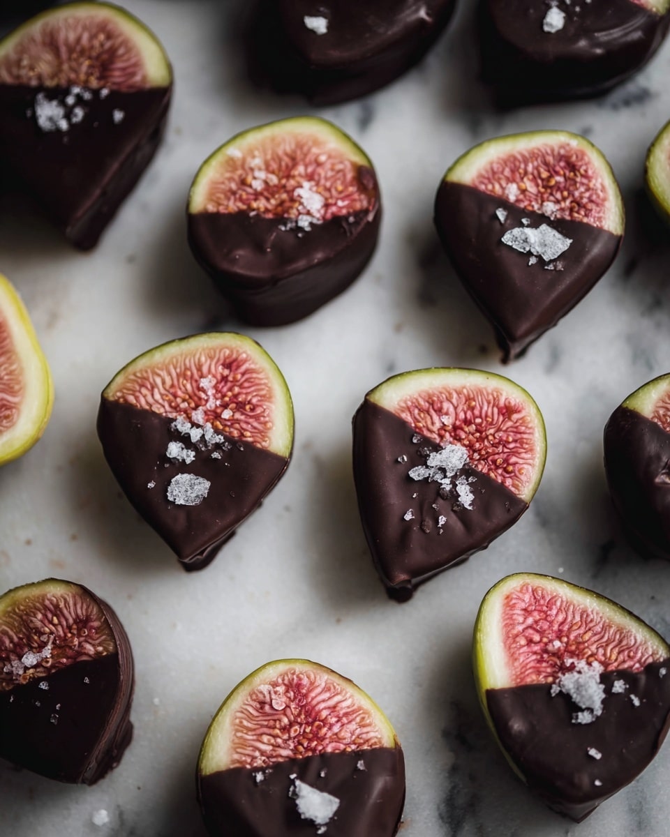 Several fig halves are arranged on a white marbled surface, each dipped halfway into dark glossy chocolate, creating a smooth, shiny dark layer that covers one side of the soft, pinkish-red seedy fig flesh and green outer skin. Flaky white sea salt is sprinkled on top of the chocolate layer, adding a rough texture contrast to the smooth chocolate. The figs are unevenly spaced, showing the mix of natural fig shapes and the even chocolate coating. Photo taken with an iphone --ar 4:5 --v 7