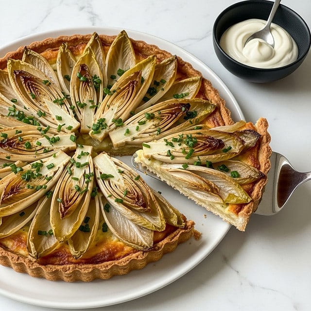 A round tart with a golden brown base topped with several layers of caramelized, soft, light brown and beige endive halves arranged in a circular pattern like flower petals, covered with finely chopped green herbs sprinkled evenly on top; one slice is being lifted with a silver spatula showing the thick, crispy crust edge and the soft, shiny endive layer, all placed on a white plate on a white marbled surface, next to a small black bowl with a dollop of white creamy sauce and a spoon. photo taken with an iphone --ar 4:5 --v 7
