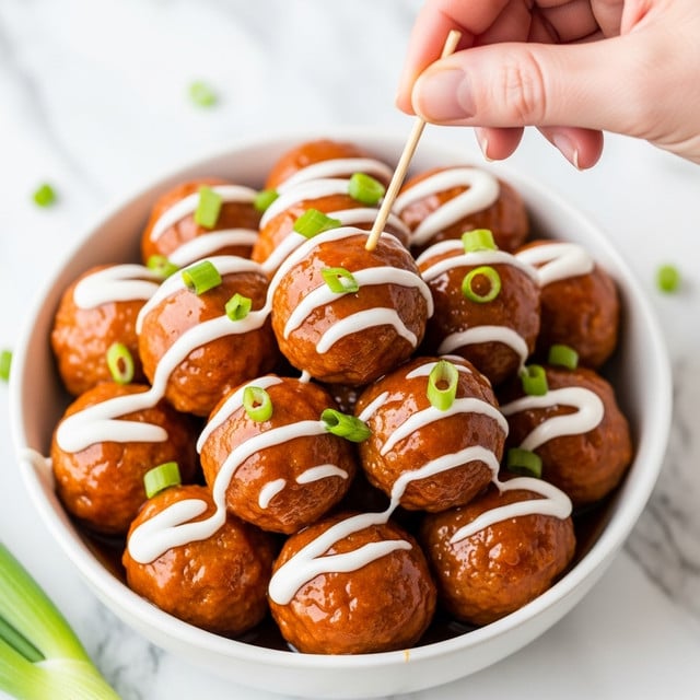 A white bowl filled with round, orange-glazed meatballs stacked closely together, each meatball covered with a shiny, smooth sauce. White creamy dressing is drizzled over the meatballs, creating soft streaks, and chopped green onion pieces are scattered on top, adding small bright green pops of color. A woman's hand is holding a thin wooden pick that is inserted into one of the meatballs near the center, lifting it slightly from the bowl. The background shows a white marbled surface with part of a green onion visible at the bottom. photo taken with an iphone --ar 4:5 --v 7