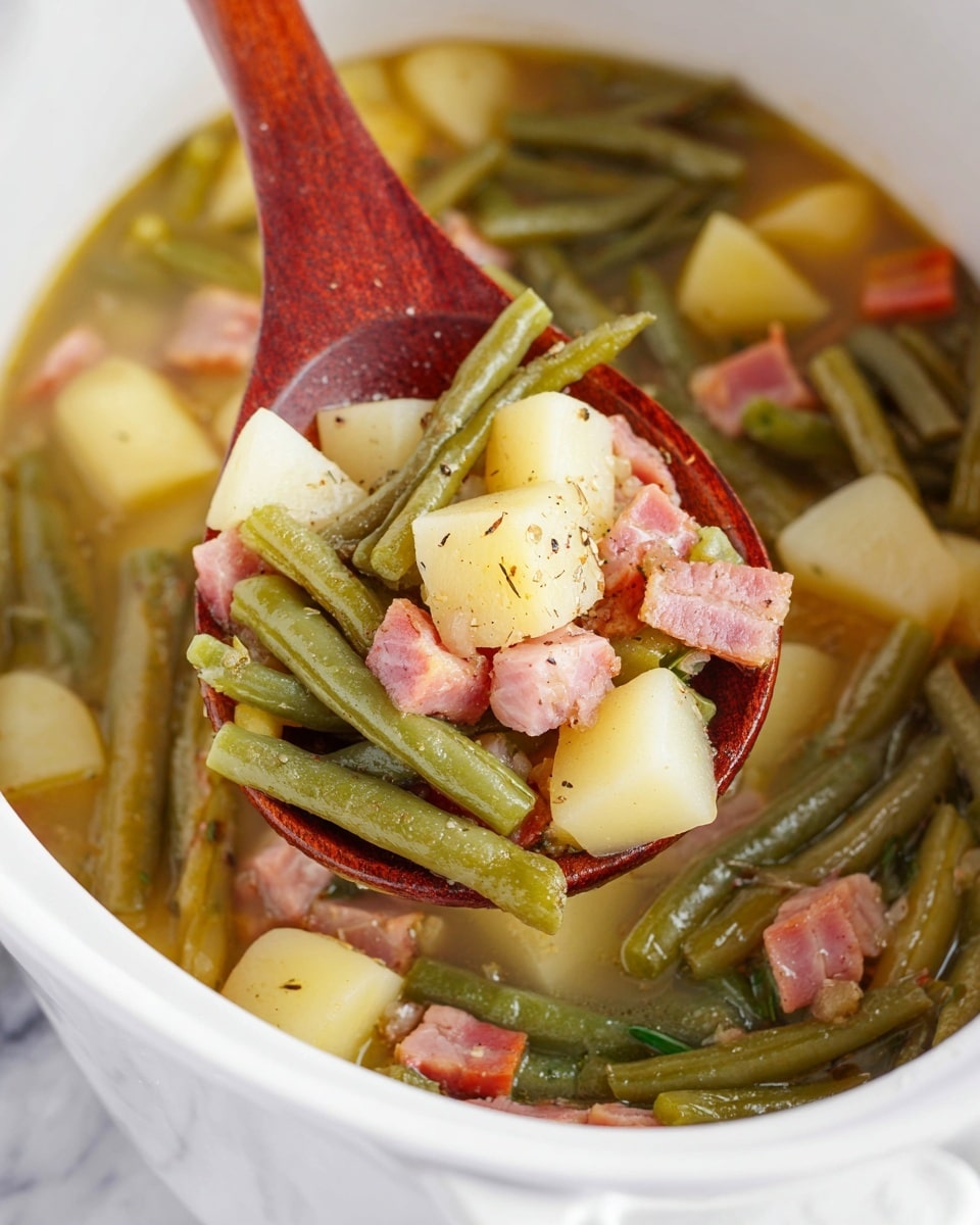 A close-up of a white pot filled with a stew-like dish showing three main layers: the bottom layer has a light broth with soft cubes of pale yellow potatoes, the middle layer contains bright green whole green beans, and the top layer features pinkish chunks of diced cooked ham sprinkled with coarse black pepper. A wooden spoon, reddish-brown in color, scoops up a mix of all layers, showing the texture and colors clearly against the white pot. The scene is set on a white marbled surface. Photo taken with an iphone --ar 4:5 --v 7