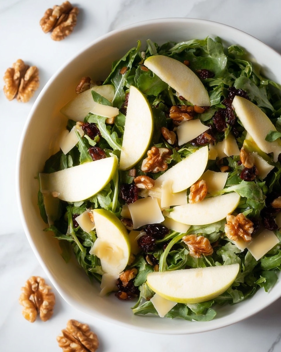 The image shows a fresh salad in a white bowl on a white marbled surface. The salad has three main layers: the base layer is dark green leafy arugula, covered by small pieces of light yellow cheese that add texture. On top, thin slices of pale green apple are neatly arranged in groups. Scattered throughout are medium brown walnut halves and small dark brown date pieces, adding contrast and richness to the salad. A few walnut pieces also rest on the surface outside the bowl. The fresh ingredients create a mix of crisp and crunchy textures. Photo taken with an iphone --ar 4:5 --v 7