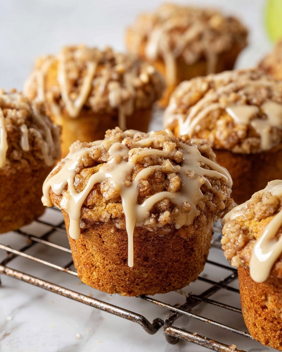 There are seven muffins on a metal cooling rack placed on a white marbled surface. Each muffin has two layers: a golden brown bottom layer and a crumbly, nut-studded top layer with a darker brown color and textured appearance. To the right of the cooling rack, there is a white bowl containing a light beige liquid, partially visible. A part of a blue and white patterned cloth is seen at the bottom right corner of the image. The lighting is soft, highlighting the muffins' texture and color. photo taken with an iphone --ar 4:5 --v 7