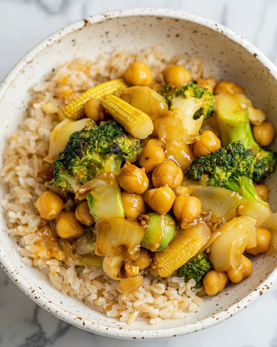 This image shows a close-up of a bowl with two layers. The bottom layer is light brown cooked rice with a slightly rough texture. On top, there is a mix of cooked vegetables and chickpeas. The vegetables include bright green broccoli florets, small yellow baby corn ribs with texture, pale yellow water chestnuts sliced into thick rounds, and pieces of soft green celery. The chickpeas are round and golden-brown with a shiny surface, mixed evenly throughout the vegetables. The dish looks warm and saucy, and the bowl is white with small brown speckles inside. The background has a white marbled texture. Photo taken with an iphone --ar 4:5 --v 7
