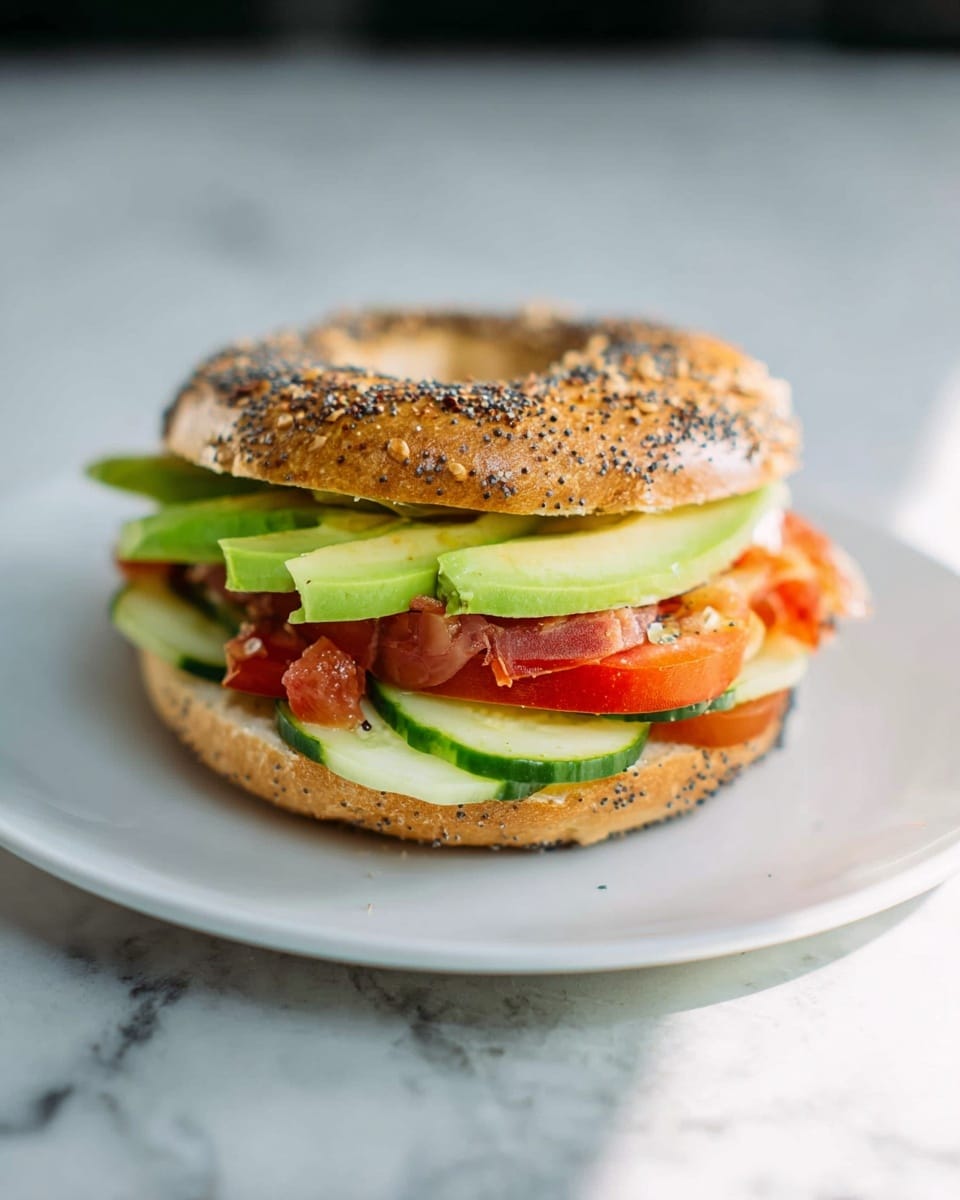 A sandwich with three main layers sits on a white plate, placed on a white marbled texture surface. The sandwich is made with a round everything bagel, light brown with visible seeds and seasoning on top. The bottom layer inside the bagel has pale green cucumber slices arranged flat, followed by a layer of bright red tomato chunks. On top of the tomato layer, there is a thick green avocado slice, adding a creamy texture. The sandwich looks fresh and colorful with natural lighting highlighting the textures and colors. photo taken with an iphone --ar 4:5 --v 7
