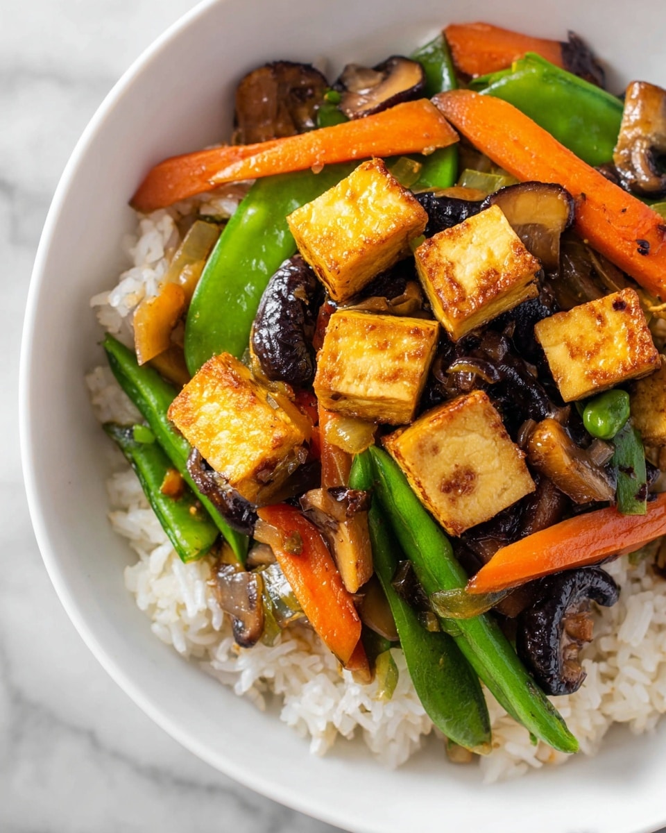 A close-up view of a white bowl filled with a three-layer dish, starting with a base of white rice with a soft, fluffy texture. On top of the rice, there is a colorful stir-fry mix made of bright orange carrot sticks, vibrant green snap peas, and dark brown sautéed mushrooms, all cooked to a tender crunch. The final top layer includes golden brown crispy tofu cubes scattered generously, adding a firm texture with slight charred edges. The bowl sits on a white marbled surface. photo taken with an iphone --ar 4:5 --v 7