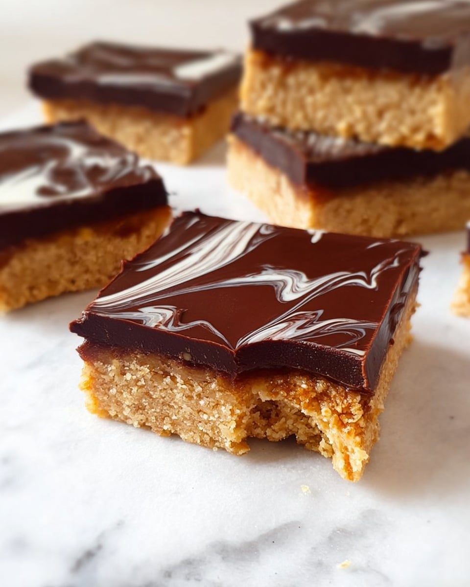 The image shows several square dessert bars arranged on a white marbled surface. Each bar has two layers: the bottom layer is a thick, crumbly, light golden-brown base with a rough texture, while the top layer is a smooth, glossy dark chocolate covering with some white swirls artfully mixed in. The front bar has a small bite taken out, revealing the soft and slightly grainy texture of the base beneath the shiny chocolate layer. In the background, bars are stacked or placed close together, emphasizing their dense, layered structure. Photo taken with an iphone --ar 4:5 --v 7