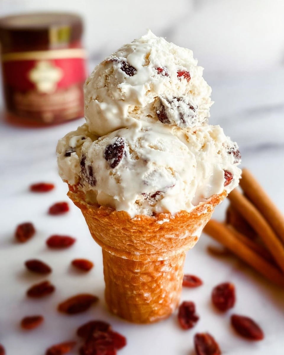 A close-up image of a single scoop of white ice cream mixed with small dark dried fruits, placed in a textured light brown waffle cone. The ice cream is piled high, showing a creamy and fluffy texture with visible chunks of the dried fruits spread throughout. Around the cone, small reddish dried fruits are scattered on a white marbled surface, with two brown cinnamon sticks blurred in the background on the right side, and a brown jar with red and beige packaging partially visible on the left side in the blurry background. Photo taken with an iphone --ar 4:5 --v 7