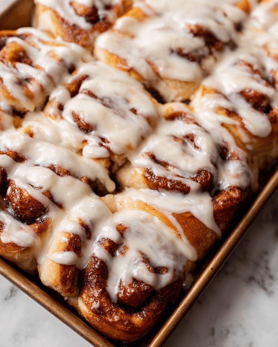 The image shows a close-up of a baking tray filled with freshly baked cinnamon rolls. Each roll has several layers of soft dough swirled with dark cinnamon filling, giving a warm brown look. The rolls are covered with thick, creamy white icing that spreads unevenly over the top, dripping down the sides to highlight the rounded and textured layers of dough. The baking tray sits on a white marbled surface, adding a clean and fresh contrast to the golden brown and white colors of the rolls. photo taken with an iphone --ar 4:5 --v 7