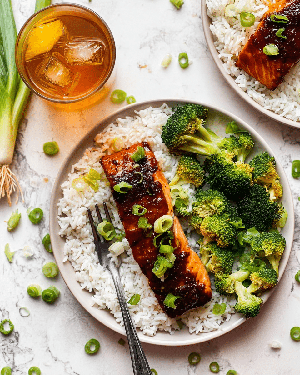 A white plate holds a food dish with three main layers: a base layer of white rice spread evenly, topped with a glazed dark brown piece of cooked salmon placed horizontally in the center, and garnished with finely sliced bright green scallions scattered on the salmon and rice. To the right side of the plate, there are fresh, bright green broccoli florets adding a vibrant contrast. A silver fork is resting on the left edge of the plate. The plate sits on a white marbled surface with some scattered green scallion slices around it. In the top left corner, there is a glass with light brown liquid and ice cubes. Photo taken with an iphone --ar 4:5 --v 7