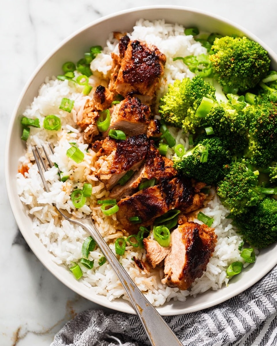 A white round plate sits on a white marbled surface, filled with fluffy white rice as the base layer. On top of the rice, several pieces of golden-brown grilled chicken are placed in the center, showing juicy, tender meat inside with a slightly charred texture on the outside. Bright green sliced scallions are scattered over the chicken and rice, adding a fresh pop of color. On one side of the plate, vibrant green steamed broccoli florets sit neatly. A silver fork rests beside the plate with a gray-striped cloth nearby. The photo looks natural and bright. photo taken with an iphone --ar 4:5 --v 7