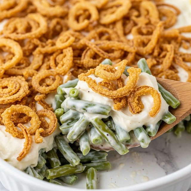 A close-up of a creamy casserole dish showing three visible layers: at the bottom, tender green beans cut into small pieces with a soft texture; the middle layer is a thick, white creamy sauce coating the green beans evenly; the top layer consists of a generous amount of crispy, golden-brown fried onion strings scattered on the surface, adding crunchy texture. A wooden spoon is scooping some of the casserole, showing the mix of all layers up close. The whole dish is set on a white marbled texture surface. Photo taken with an iphone --ar 4:5 --v 7