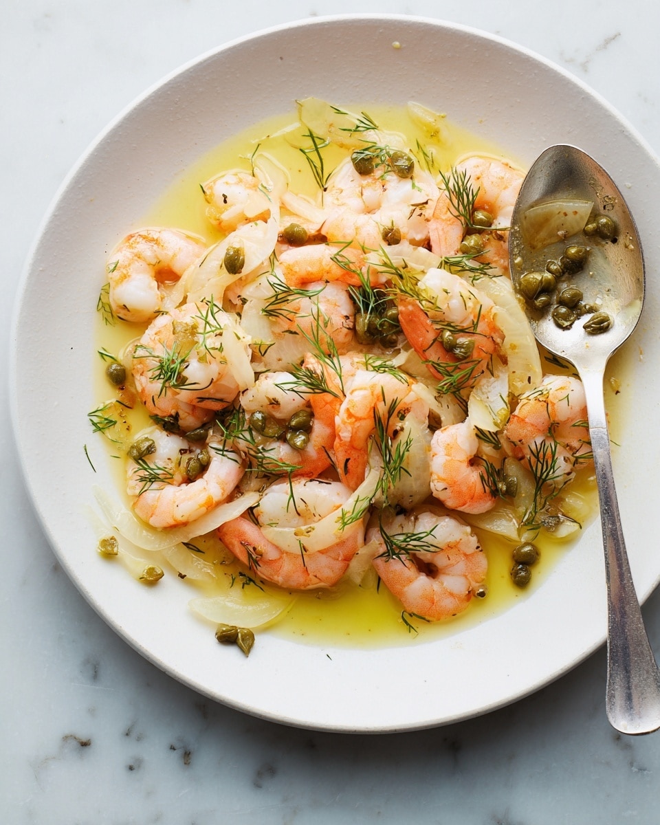 A white plate holds a dish made of shrimp in a light yellow sauce. There are about two layers of shrimp that are pink with white flesh and slight orange edges, spread evenly across the plate. Mixed in are thin, pale slices of onion or fennel and small green capers scattered around. Fresh small dill leaves add a touch of green scattered over the shrimp. A silver spoon rests on the right side of the plate, partially covered with sauce and small herbs. The plate is on a white marbled surface. Photo taken with an iphone --ar 4:5 --v 7