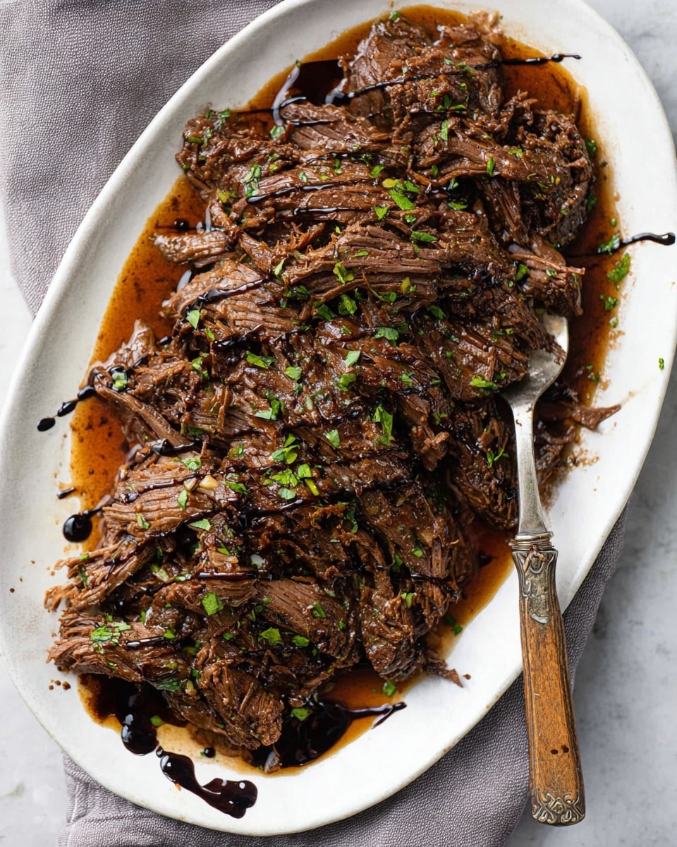 A white oval plate holds a generous pile of shredded dark brown beef, showing a moist and tender texture with visible grain and small bits of green herbs scattered evenly on top. The beef is coated lightly in a shiny, rich brown sauce that pools at the bottom of the plate, with thick black drizzle sauce spread irregularly over the meat's surface. A vintage fork with a wooden handle rests on the right side of the plate, partially submerged in the sauce. The dish sits on a white marbled surface with a soft gray linen napkin nearby. Photo taken with an iphone --ar 4:5 --v 7