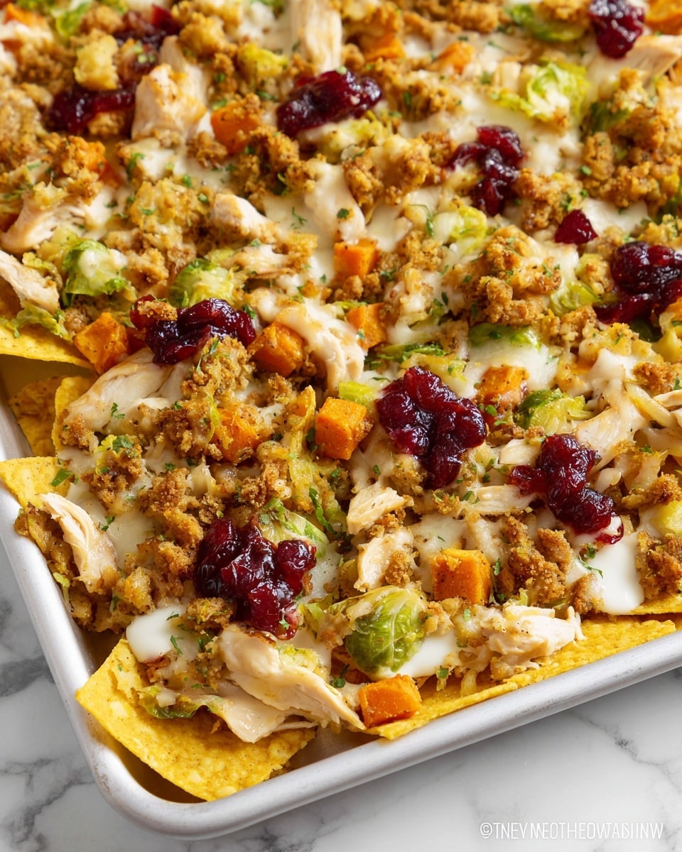 A large pile of nachos sits on a white plate, layered with crispy yellow tortilla chips at the bottom, topped with shredded light brown turkey and chunky beige stuffing mixed with small green and orange vegetable pieces. Scattered dark red dried cranberries and a smooth, glossy brown gravy are drizzled all over, with a sprinkle of green herbs on top. The edges of the pile also have some small green leaves as garnish, all placed on a white marbled surface with blurred background plates and a jar of dark red sauce nearby. Photo taken with an iphone --ar 4:5 --v 7