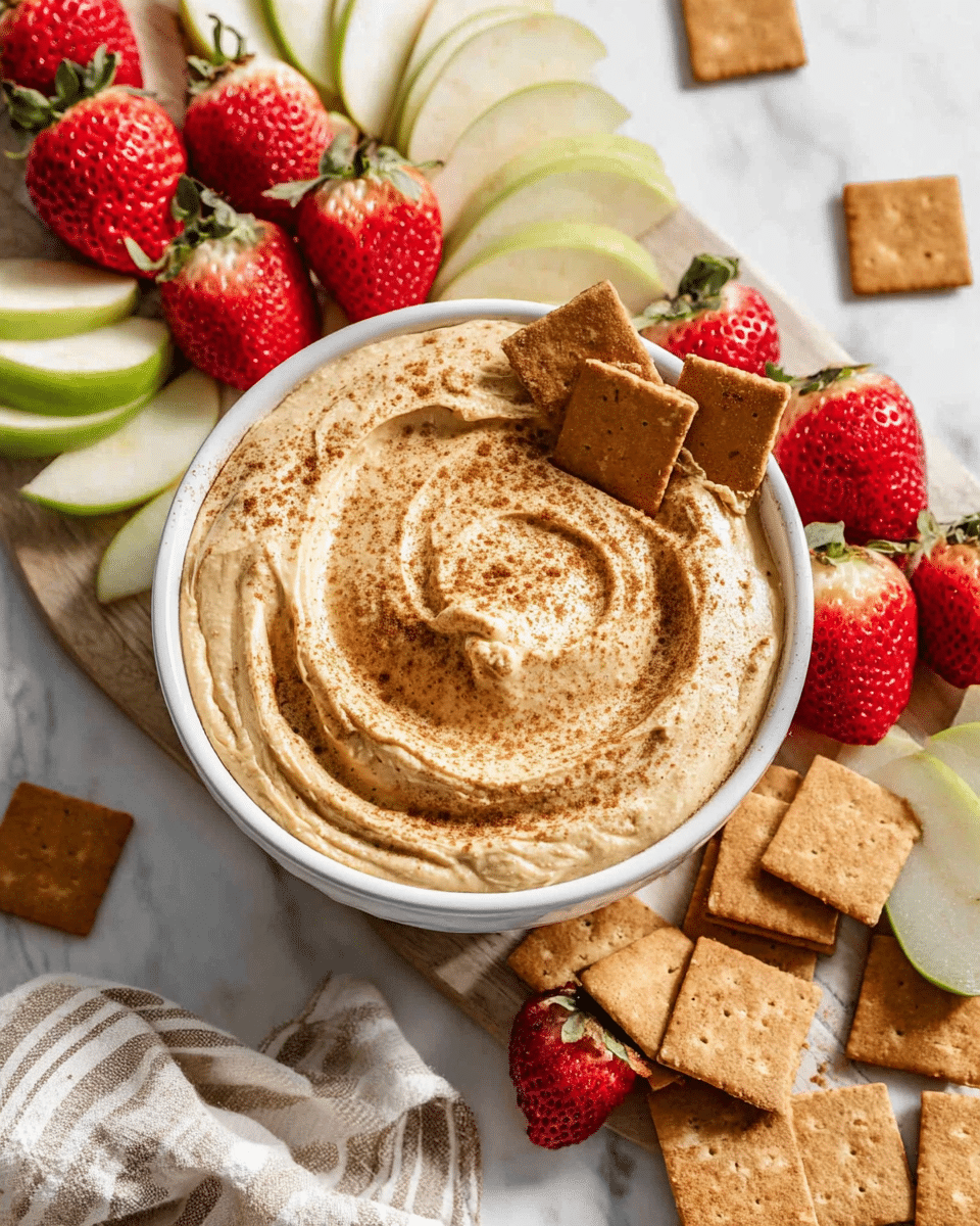A white bowl filled with a thick, creamy dip that is light tan in color with a smooth, slightly swirled surface, sprinkled with a fine dusting of cinnamon on top. Three square, brown crackers are partially dipped into the smooth layer near the center of the bowl. The bowl rests on a light wooden board surrounded by fresh, bright red strawberries with green tops, some whole and some halved, and green apple slices arranged in neat layers on both sides. Additional square brown crackers are scattered on a white marbled surface beside the board. In the lower part of the image, a beige and white striped cloth is partly visible. Photo taken with an iphone --ar 4:5 --v 7