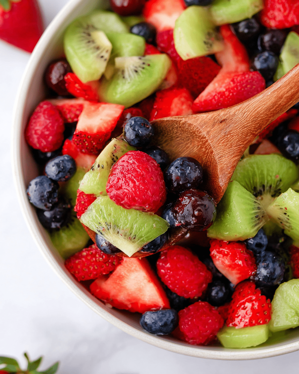 A close-up view of a white bowl filled with a colorful fruit salad, showing three layers of mixed fruit: red raspberries and sliced strawberries with their textured seeds and bright red color, dark blue shiny blueberries scattered through the bowl, and green sliced grapes along with smooth light green kiwi pieces that have black seeds. A wooden spoon is partially visible, scooping some fruit from the bowl, all against a white marbled surface background. The photo captures the freshness and varied textures of the fruits in bright natural light. Photo taken with an iphone --ar 4:5 --v 7