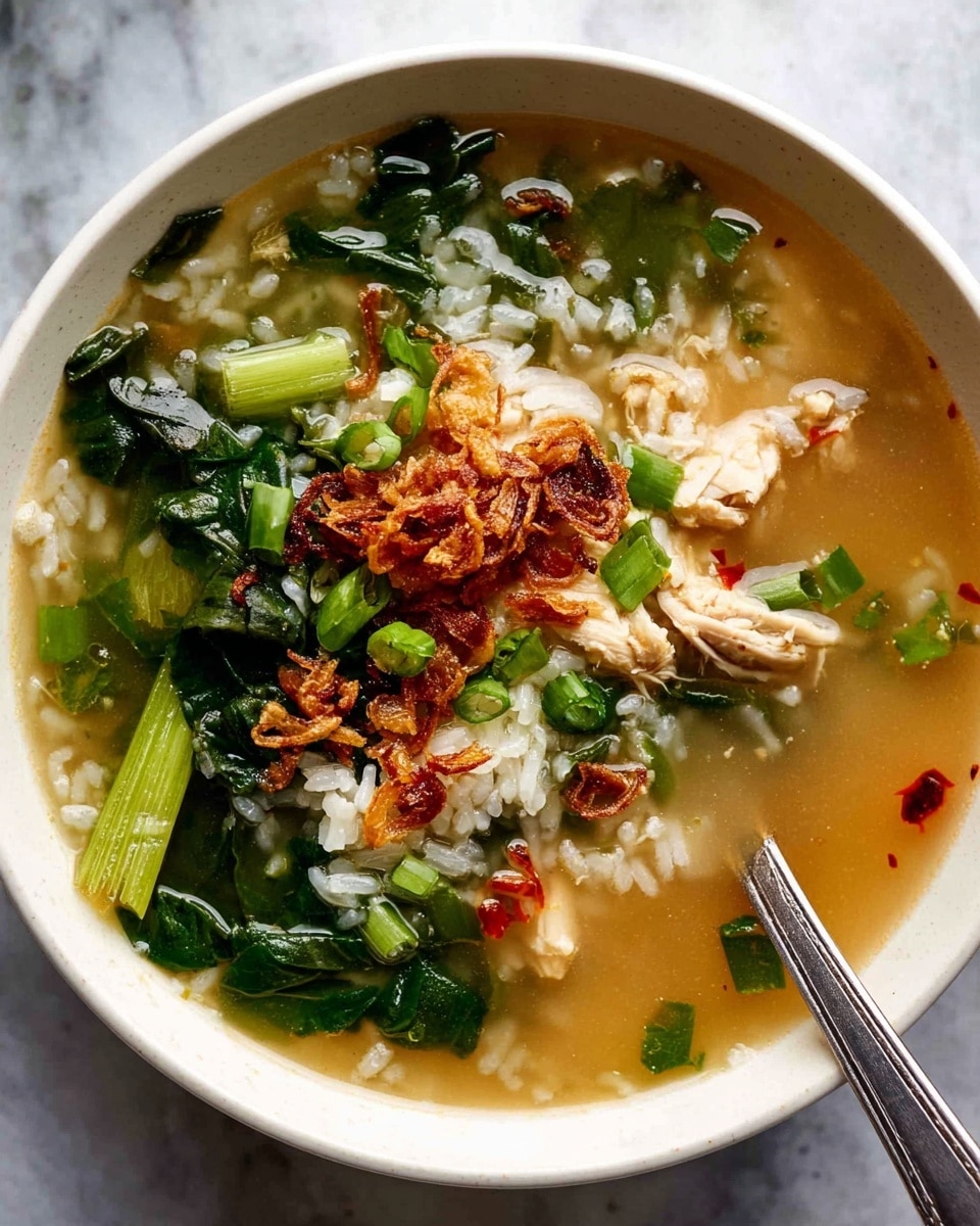 A white bowl filled with a clear broth soup containing three main layers: at the bottom, scattered white rice grains partially submerged in the light brown broth; in the middle, chunky pieces of cooked chicken and bright green leafy vegetables with some stalks placed around the edges; on top, sprinkled crispy fried shallots and chopped green onions with small drops of red chili oil floating on the surface. The bowl is placed on a white marbled surface, with a metal spoon resting inside the bowl on the right side. Photo taken with an iphone --ar 4:5 --v 7