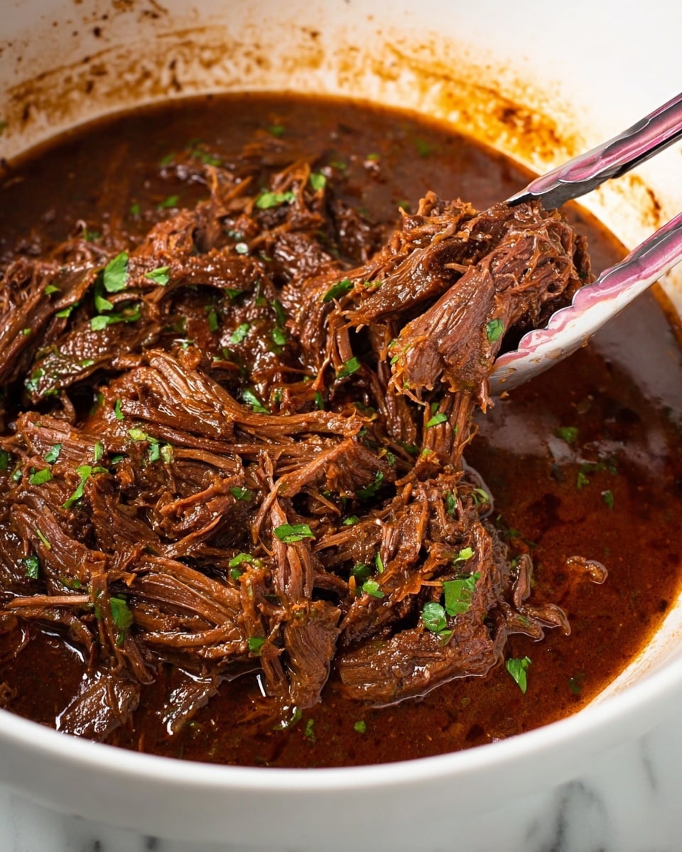 Inside a white bowl, there is a rich, dark brown shredded meat stew with a thick, glossy sauce. The meat looks tender and stringy with bits of green herbs scattered on top for garnish. Pink and silver tongs hold a portion of the meat, lifting it slightly above the sauce. The edges of the bowl show some splashes of the sauce, adding to the rustic look. The bowl is placed on a white marbled surface. photo taken with an iphone --ar 4:5 --v 7