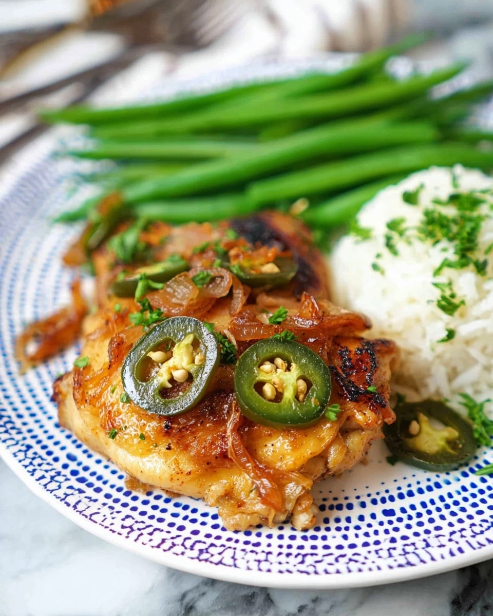 The image shows a white plate with a blue dotted pattern holding a cooked chicken thigh in the center. The chicken has a golden-brown, crispy skin with small pieces of caramelized onions on top and several slices of green and dark green jalapeños scattered over it. To the right of the chicken, there is a small mound of white rice with some chopped green herbs sprinkled on it. Behind the chicken and rice, a bunch of bright green cooked green beans are neatly arranged in a row. The plate sits on a white marbled surface, and a fork is visible in the background. photo taken with an iphone --ar 4:5 --v 7