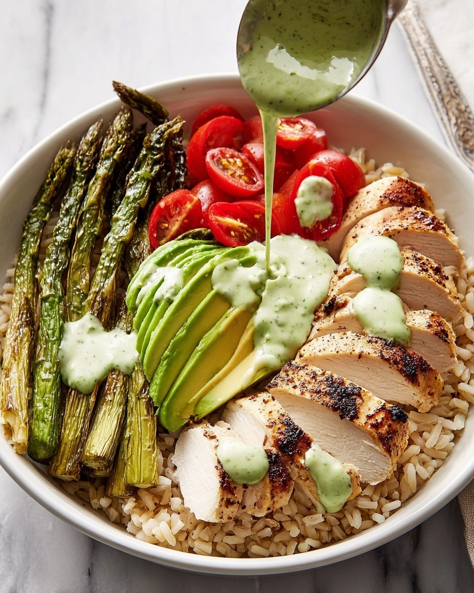 A white bowl filled with a base layer of light brown cooked rice, topped with three main sections: sliced grilled chicken breast on the right, showing a golden-brown crust with tender white inside, roasted green asparagus spears in the middle with slight char marks, and fresh red cherry tomato halves along with bright green avocado slices on the left. A creamy green sauce is drizzled smoothly over the chicken, asparagus, tomatoes, and avocado. In the background, there is a spoon pouring more of the green sauce onto the chicken, all set on a white marbled surface. photo taken with an iphone --ar 4:5 --v 7