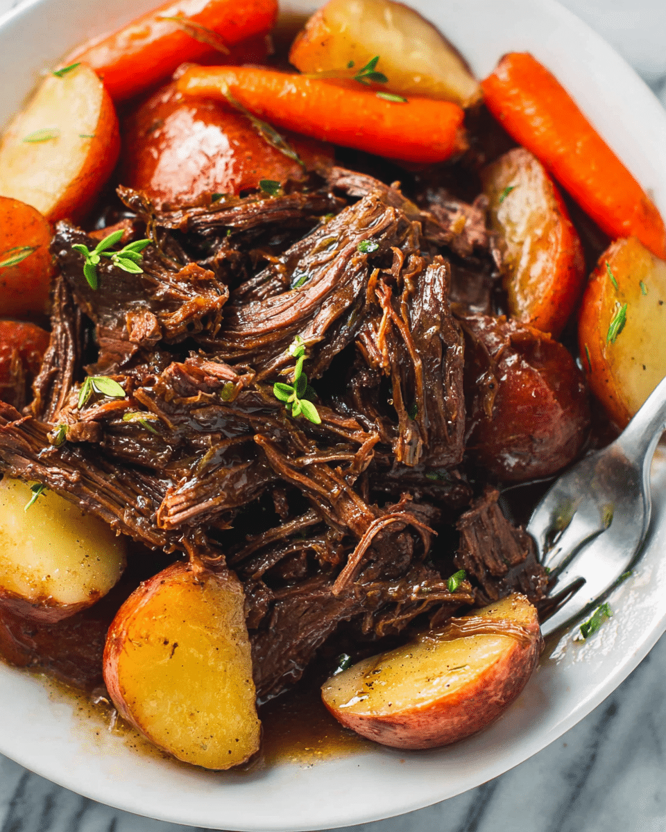 The image shows a close-up of a white plate filled with tender, shredded beef pieces that are dark brown and juicy, with a glossy texture from the gravy coating. Surrounding the beef are chunks of red-skinned potatoes that are light yellow inside and baby carrots that are bright orange, both cooked but still holding shape. Small green sprigs are placed as a garnish on top of the beef, adding a touch of fresh color. A metal fork is placed on the right side of the plate. The plate sits on a white marbled texture. Photo taken with an iphone --ar 4:5 --v 7