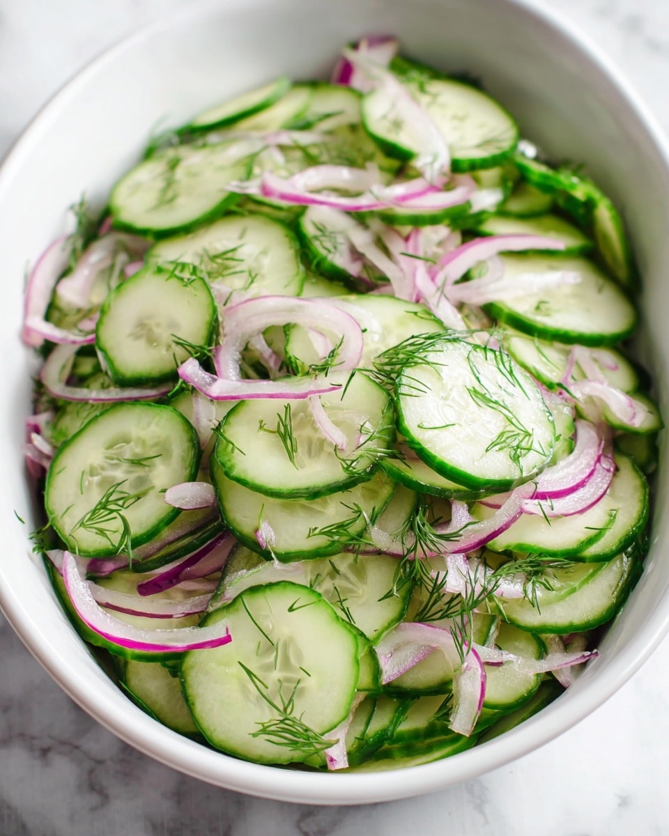 A white oval bowl is filled with a fresh cucumber salad composed of thin green cucumber slices that have a slightly translucent center, mixed with thinly sliced purple-red onion strips scattered evenly throughout. Small green dill leaves are sprinkled on top, adding brightness and a delicate texture contrast. The cucumber slices are layered loosely, creating a light and airy appearance with a mix of round shapes and slight overlaps. The background is a white marbled texture. photo taken with an iphone --ar 4:5 --v 7