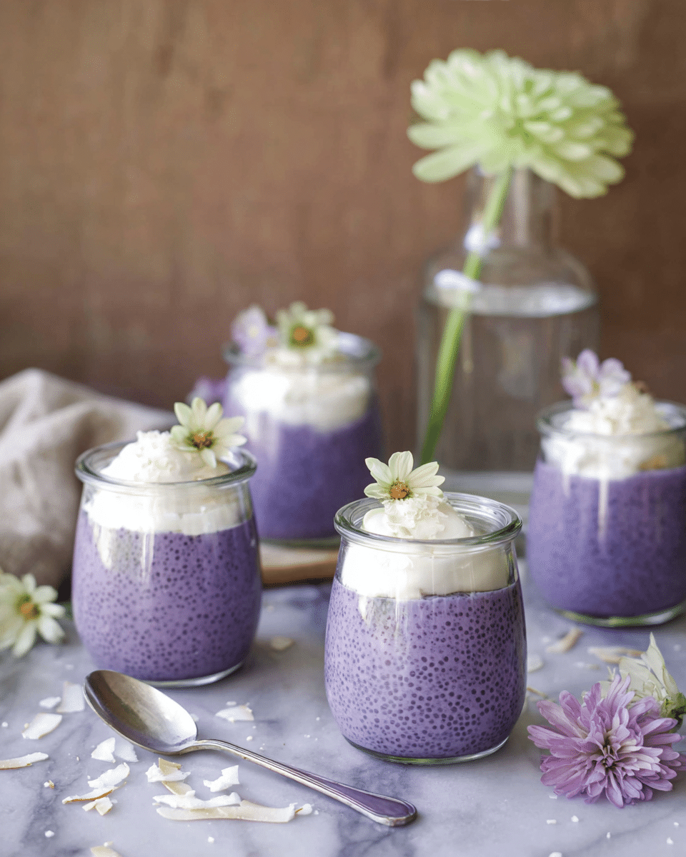 Four small glass jars hold a two-layer dessert arranged on a white marbled surface. The bottom layer is thick and purple with a dotted texture, filling most of each jar. On top is a smooth, fluffy white cream layer, with two jars garnished with a small pale green flower. A silver spoon lies beside two jars, and light purple flowers and white toasted coconut flakes are scattered around. In the background, there is a clear glass vase with water and a pale green flower, set against a soft brown blurred backdrop. photo taken with an iphone --ar 4:5 --v 7