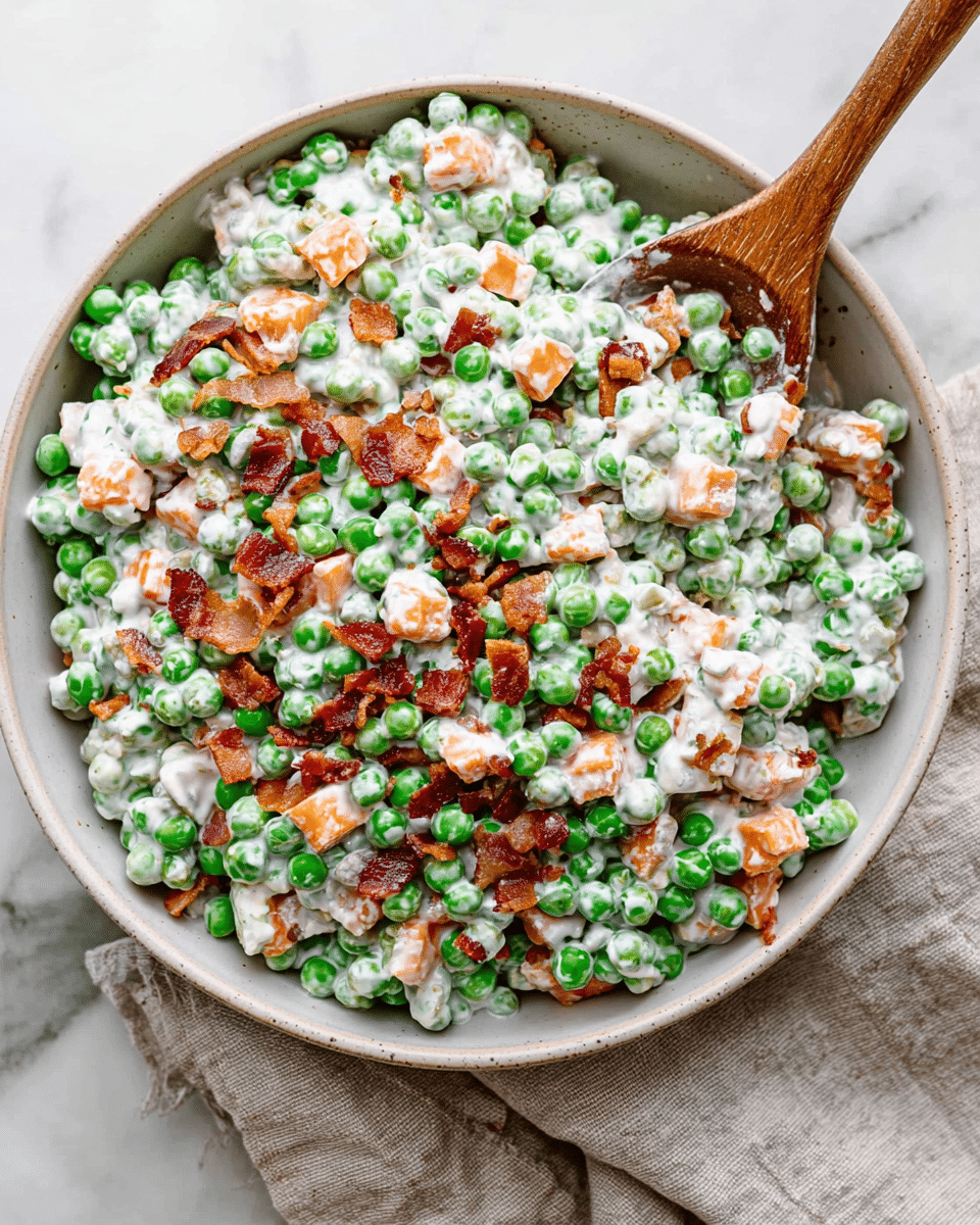 A white bowl filled with a creamy pea salad made of bright green peas coated in a thick white dressing. Mixed within are small cubes of light orange cheese and scattered pieces of crispy brown bacon. The salad looks fresh and textured with layers of cream, green peas, orange cheese, and bits of bacon on top. A wooden spoon is placed inside the bowl on the right side, partially lifting some of the salad. The bowl is set on a soft beige cloth over a white marbled surface. Photo taken with an iphone --ar 4:5 --v 7