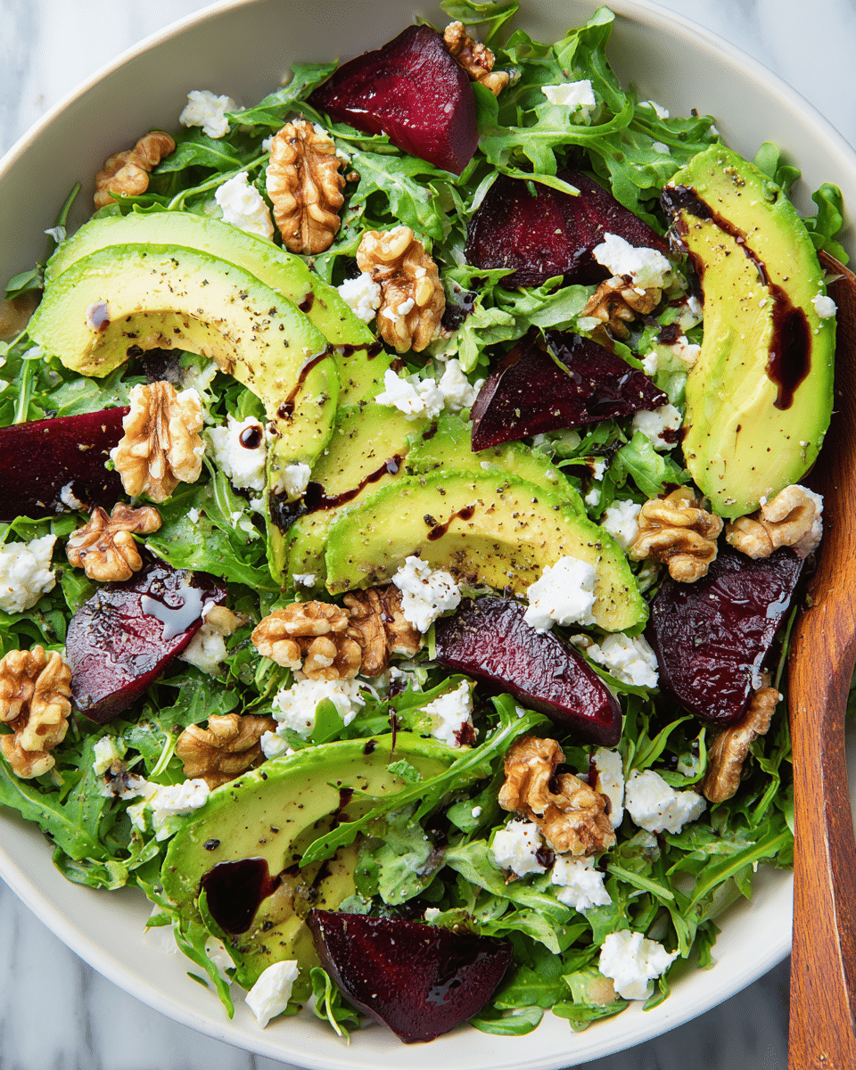 This image shows a fresh salad in a white bowl filled with vibrant green arugula leaves as the base layer. On top, there are deep purple beet slices cut into wedges, creamy light green avocado slices scattered evenly, and rough pieces of brown walnut adding texture. Small white crumbles of goat cheese are sprinkled over everything. The salad is lightly drizzled with dark balsamic vinegar drops, and some black pepper is visible on the avocado. The bowl is placed on a white marbled surface, and a wooden spoon peeks from the right side. photo taken with an iphone --ar 4:5 --v 7