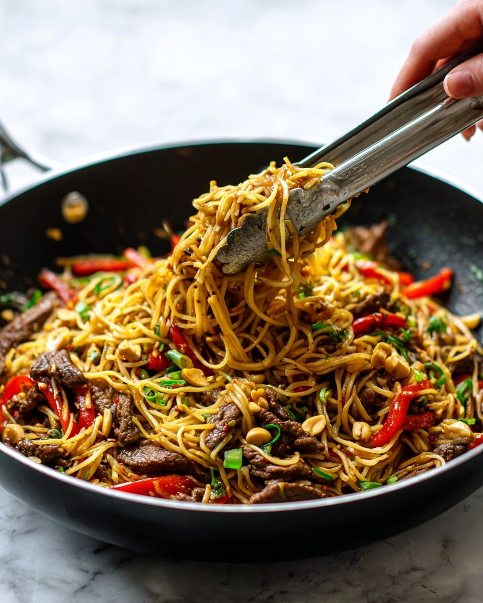 A close-up view of a black pan filled with cooked thin noodles mixed with small pieces of brown beef and bright red bell peppers. Scattered peanuts add a light tan color, while small green onion slices bring a splash of green. A woman's hand is holding silver tongs, lifting a portion of the noodles and beef from the pan. The noodles are shiny and slightly oily, winding through the ingredients, giving the dish a textured and colorful look. The photo has a bright and natural light on a white marbled texture background. photo taken with an iphone --ar 4:5 --v 7
