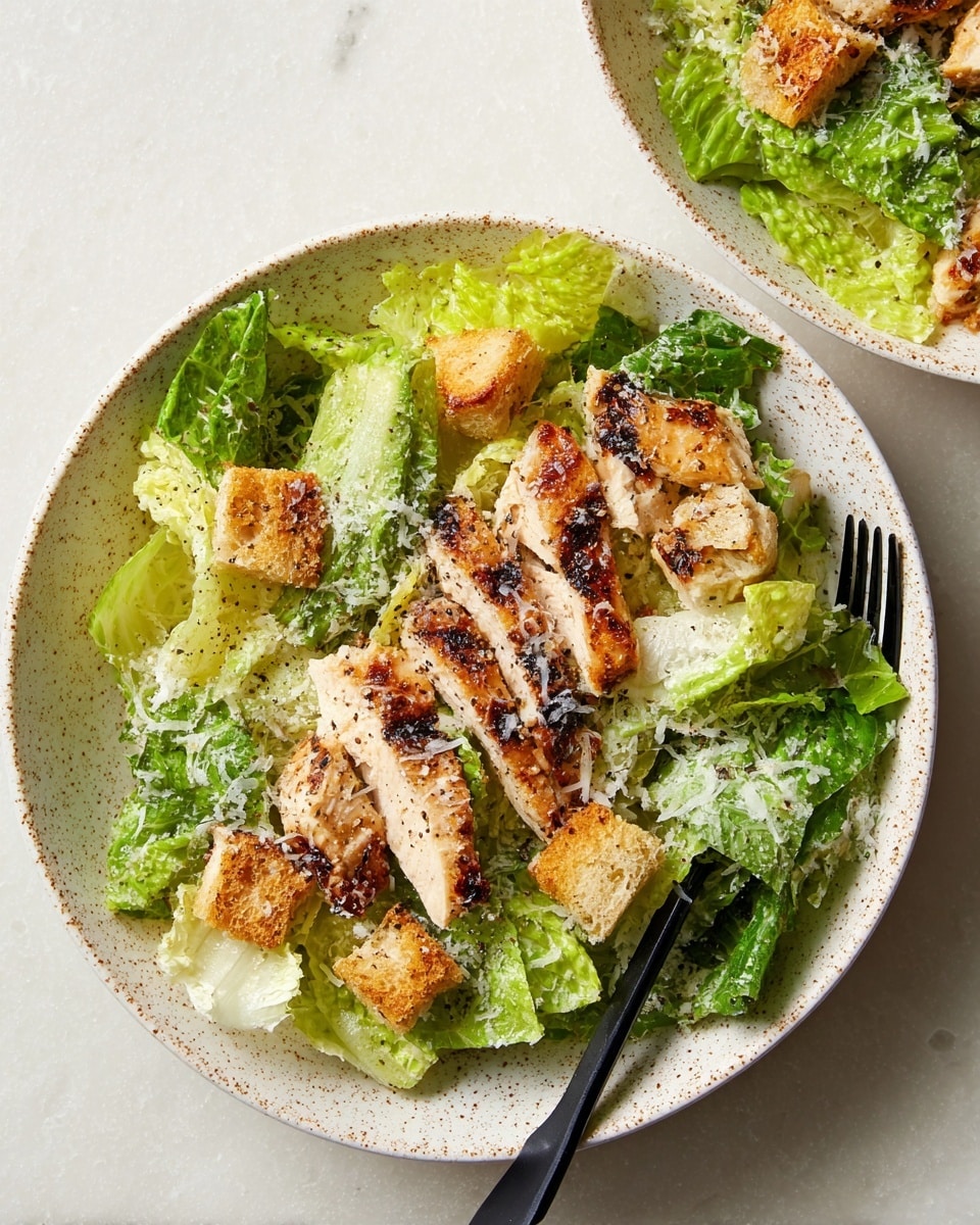 A close-up of a grilled chicken Caesar salad served in a white plate with a speckled rim. The first layer shows fresh light to medium green romaine lettuce leaves covering the plate. On top, there are several charred, golden-brown grilled chicken strips arranged in the center. Scattered around the chicken are crunchy golden crouton pieces. The whole dish is lightly sprinkled with finely grated white cheese and black pepper. A black fork rests on the right side of the plate, slightly touching the lettuce. The plate is placed on a white marbled texture surface. Photo taken with an iphone --ar 4:5 --v 7