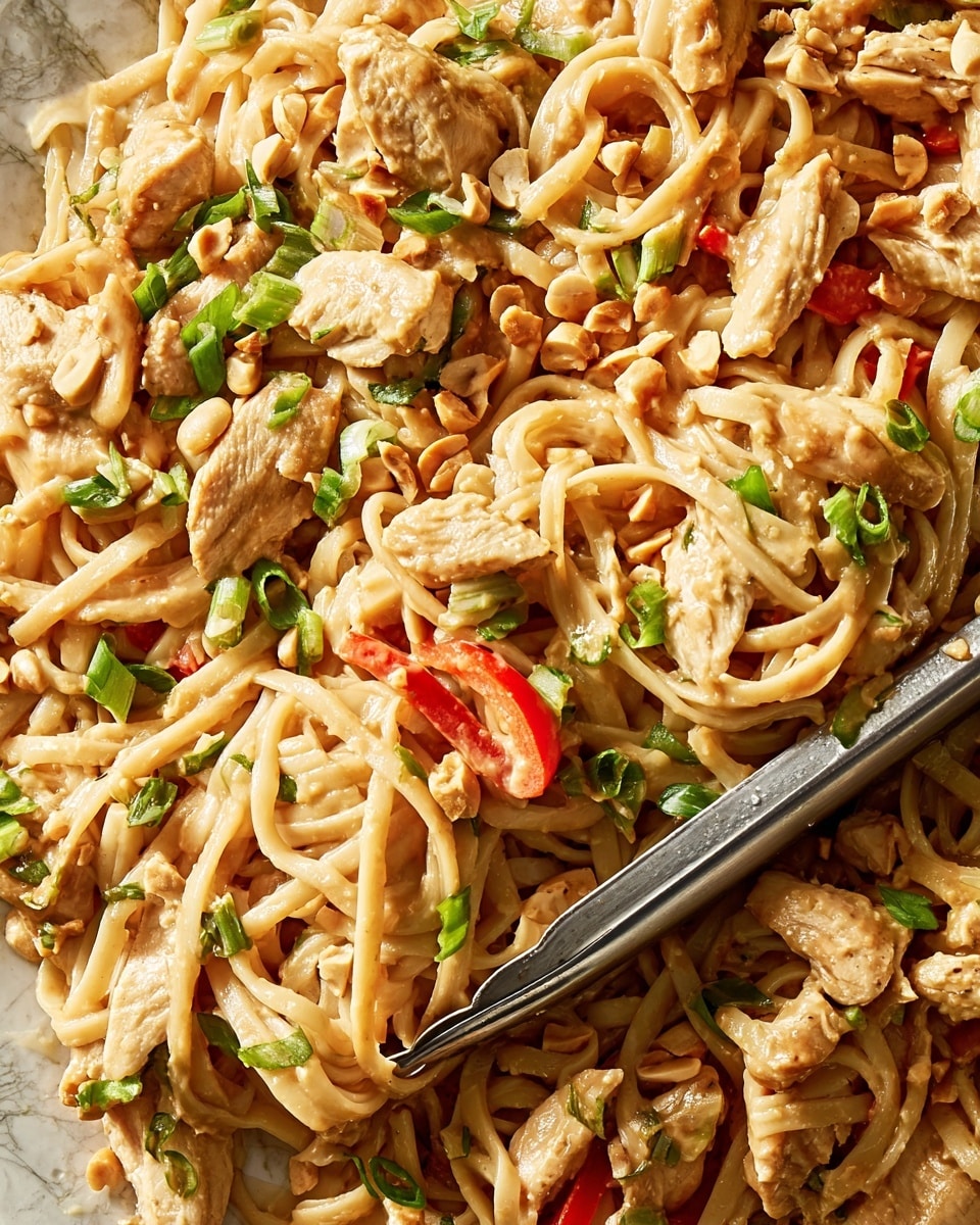 A close-up view of a large serving of noodles mixed with strips of cooked chicken and slices of red bell pepper. The noodles are creamy beige in color and look soft, coated with a smooth, light brown peanut sauce. Chopped green onions and small pieces of crushed peanuts are sprinkled evenly on top, adding touches of bright green and light tan. The texture is rich and saucy, with the chicken pieces showing a slight golden brown sear. A metal tong is placed slightly off-center among the noodles, ready for serving. The whole dish rests on a white marbled texture surface. photo taken with an iphone --ar 4:5 --v 7