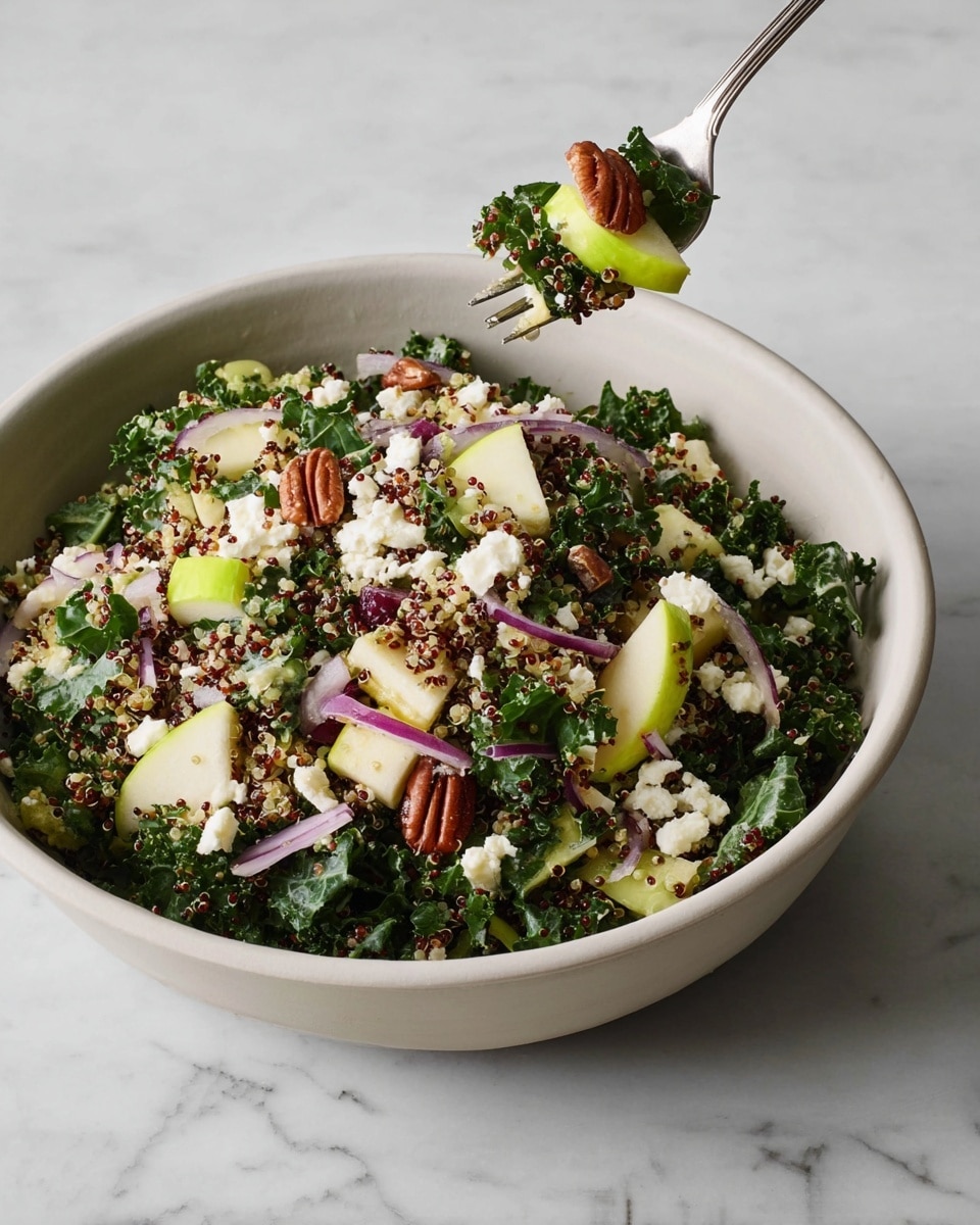 A large white bowl filled with a colorful salad showing four main layers: the bottom layer made of dark green curly kale leaves, mixed with small white and reddish quinoa grains scattered throughout; the middle layer has chunks of pale green apple pieces and thin slices of purple-red onion spread evenly; topping the salad are white crumbles of soft cheese and small brown pecans placed on the top; above the bowl, a metal fork holds a small bite of the salad with a few kale leaves, a green apple chunk, a pecan, and a bit of white cheese. The background and surface are a white marbled texture. photo taken with an iphone --ar 4:5 --v 7