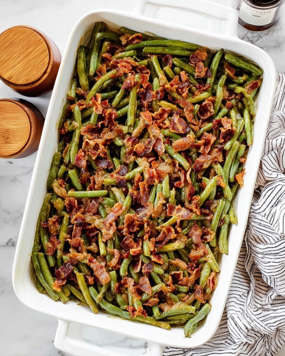 A white rectangular dish is filled with one layer of cooked green beans topped evenly with a layer of crispy brown bacon pieces. The green beans are a mix of bright and dark green colors with a soft texture, while the bacon pieces are curled and crunchy, scattered all over the top. The dish sits on a white marbled surface, next to two small round containers with wooden lids and a striped cloth partly visible in the frame. photo taken with an iphone --ar 4:5 --v 7
