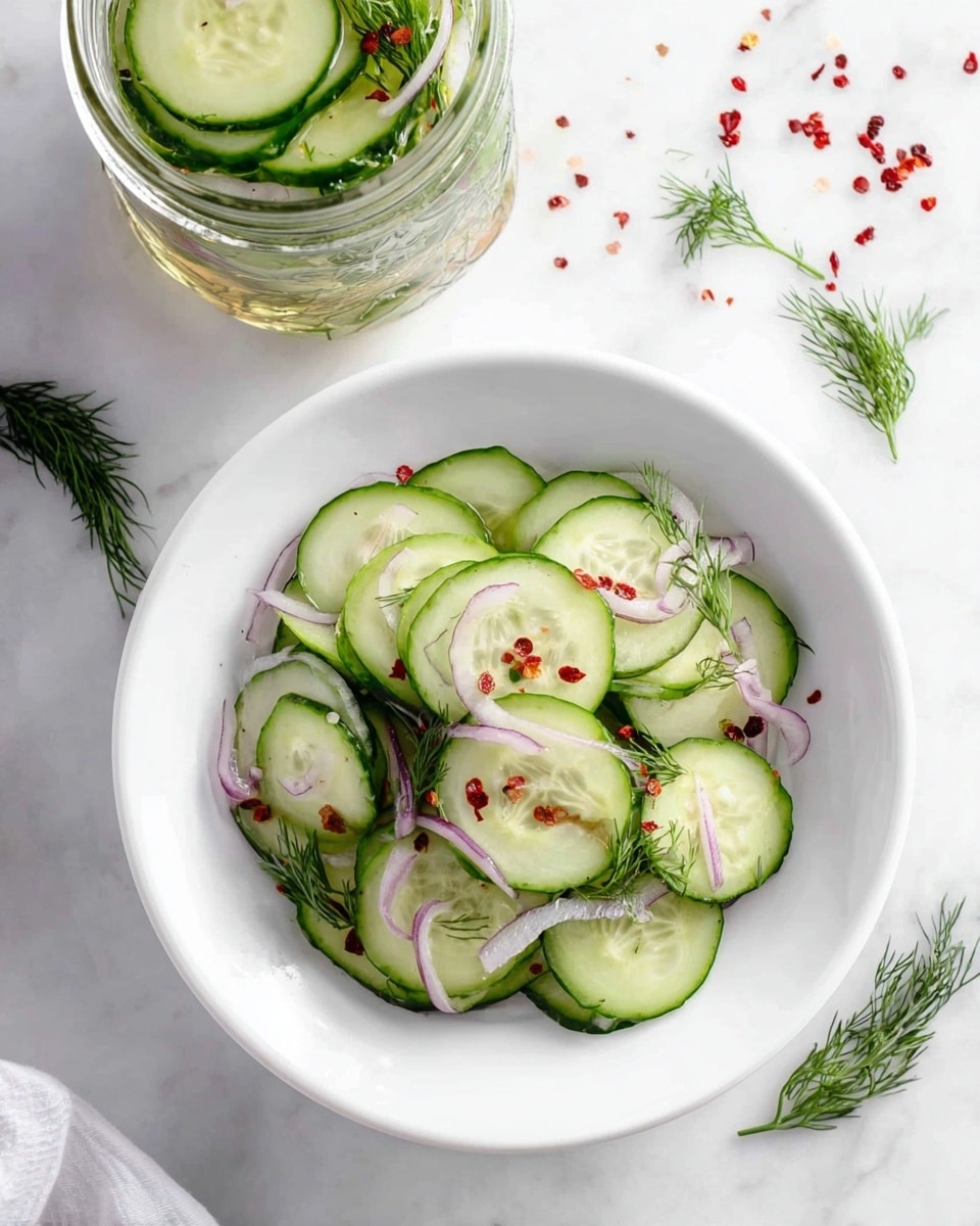 The image shows a white bowl filled with thinly sliced cucumber rounds as the base layer, mixed with thin slices of pale purple onion layered on top. Small green dill sprigs are scattered throughout the salad, adding texture and color. Tiny red pepper flakes and seeds are sprinkled gently over the cucumber slices for a touch of color and detail. At the top left corner, there is a glass jar filled with the same salad ingredients submerged in liquid. The whole scene is set on a white marbled surface, with some loose red pepper flakes and fresh dill sprigs placed around for decoration. photo taken with an iphone --ar 4:5 --v 7