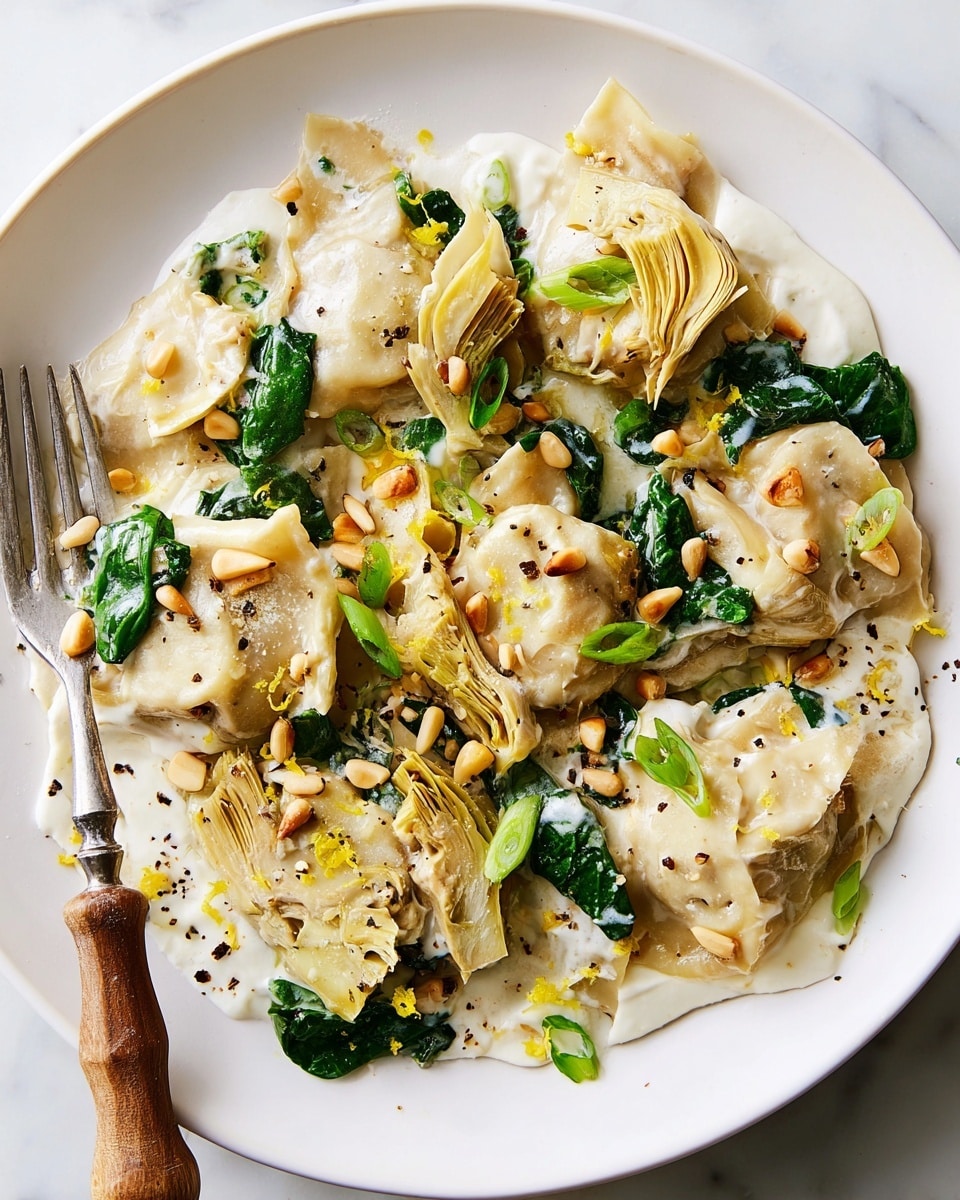 The dish shows a white round plate filled with about three layers of food. The bottom layer is creamy white sauce with smooth texture. On top of the sauce, there are large pieces of pale beige pasta filled and folded, some of them showing a soft green vegetable inside. Mixed among the pasta are dark green spinach leaves and pale yellow pieces of artichoke. Scattered on top are small, shiny, golden brown pine nuts and finely chopped bright green scallions. The whole dish is lightly sprinkled with black pepper and lemon zest, adding small yellow specks. A silver fork with a wooden handle is placed on the left edge of the plate. The plate is set on a white marbled surface. photo taken with an iphone --ar 4:5 --v 7
