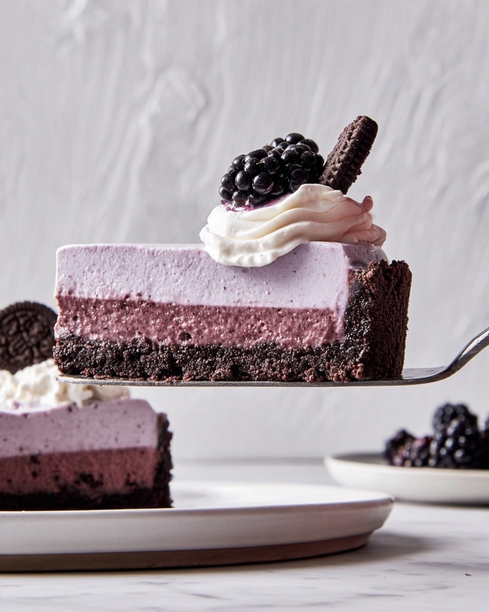 A close-up side view of a slice of berry mousse tart held on a silver spatula, showing three layers: a dark brown crumbly chocolate crust base, a thick light purple mousse middle layer, and a small dollop of white cream topping with a purple swirl. On top of the cream are two fresh blackberries and a small piece of chocolate cookie. The remaining tart sits on a white plate in the background, topped with extra cream and blackberries. The scene is set against a white marbled textured surface and wall. Photo taken with an iphone --ar 4:5 --v 7