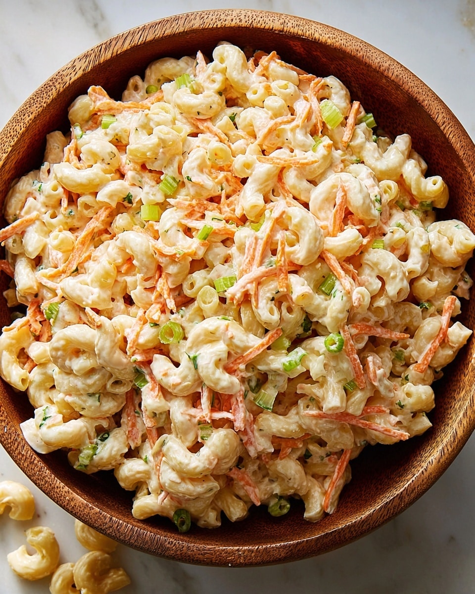 The image shows a wooden bowl filled with creamy macaroni salad placed on a white marbled surface. The salad is made of three main layers mixed together: soft, pale-yellow elbow macaroni coated in a shiny, white mayonnaise dressing, thin orange carrot strips scattered evenly throughout, and small green pieces of celery sprinkled on top for color and texture. The pasta looks moist and smooth, the carrot strips are slightly crunchy, and the celery adds a fresh touch. Some macaroni pieces have spilled beside the bowl, adding a casual feel. The photo taken with an iphone --ar 4:5 --v 7