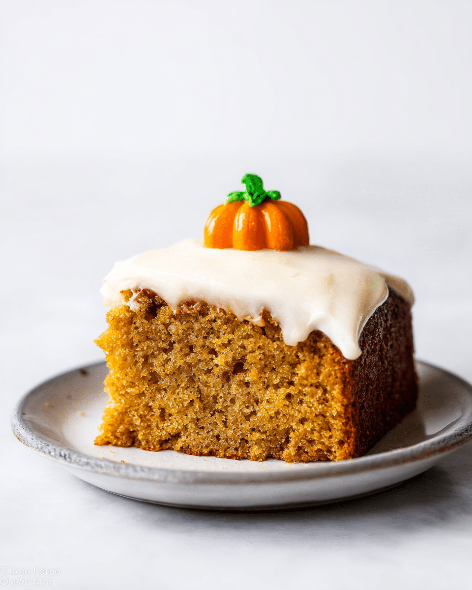A single thick slice of moist golden-brown cake with a rough, slightly porous texture sits on a white plate. The cake is topped with a smooth, creamy layer of white frosting that slightly drips over the edges. On top of the frosting, toward the back center, is a small, detailed decoration resembling an orange pumpkin with a green stem. The setting is a clean white marbled surface with a bright, plain white background. photo taken with an iphone --ar 4:5 --v 7
